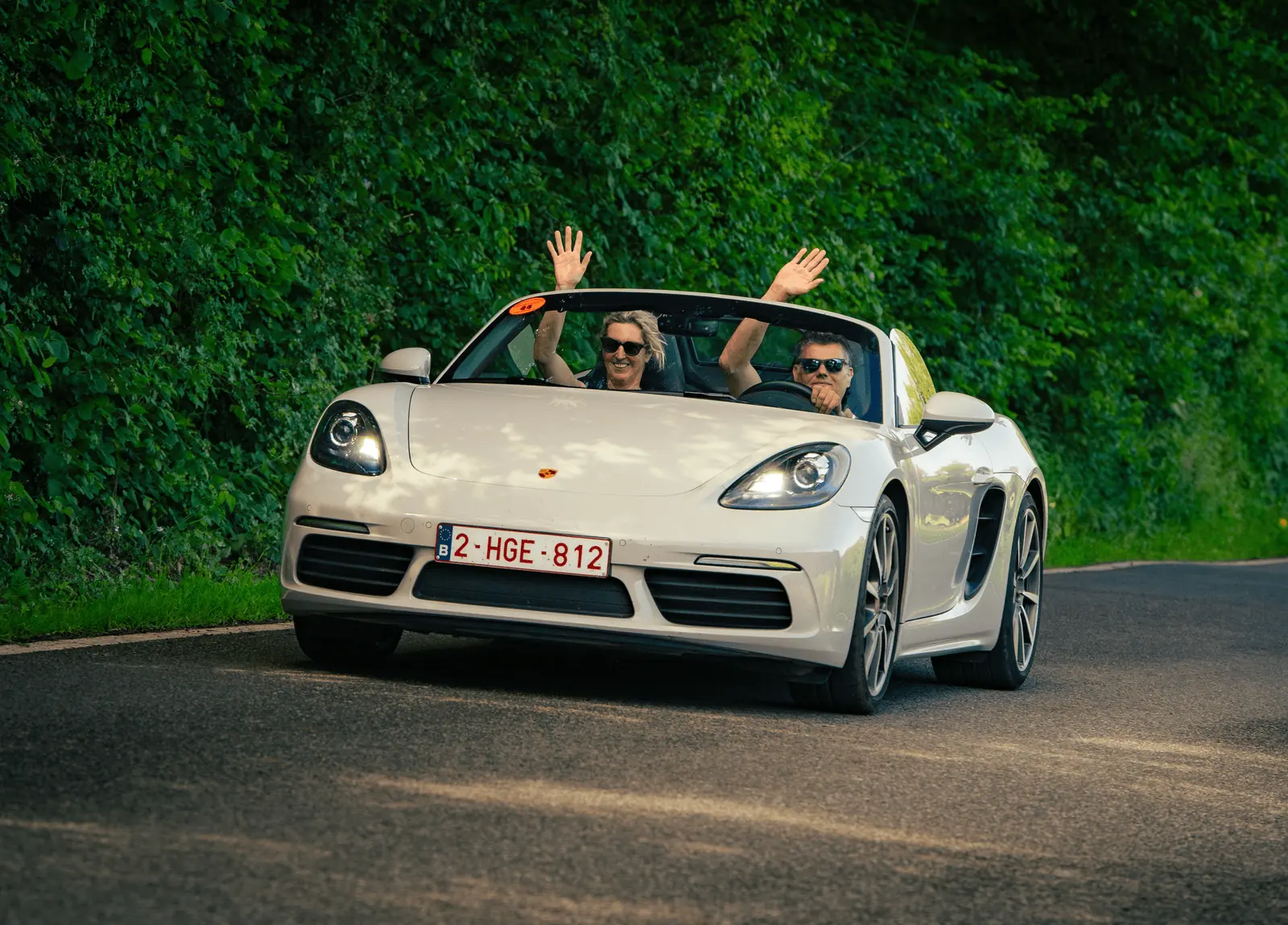 Deelnemers zwaaien vanuit een open Porsche